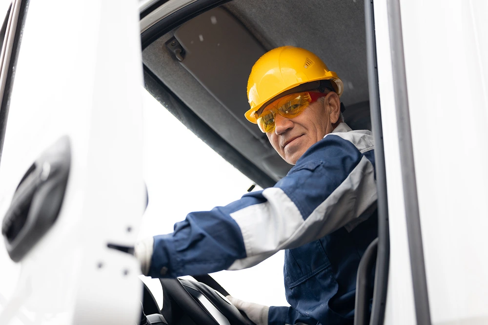 Happy driver man of industrial dump truck sits in cab and works on construction building site