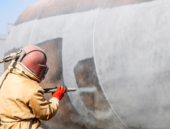 man sandblasting a holding tank